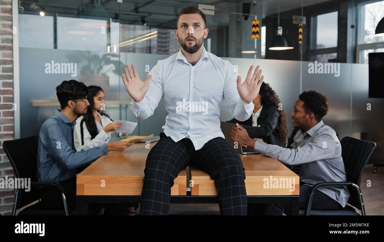 Müder Mann, männlicher Geschäftsführer, Geschäftsführer eines Unternehmens, sitzt auf einem Tisch im Büro und hält sich in der Geste des vorderen Stopps an den Händen und legt eine Idee für den Hintergrund vor Stockfoto