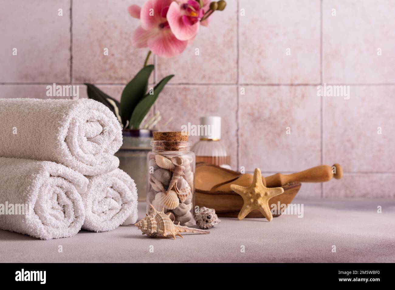 Weiße Handtücher, Holzschüssel, Muscheln, Orchideenblume und Parfüm zum Entspannen, Bad, Spa auf Fliesenhintergrund Stockfoto