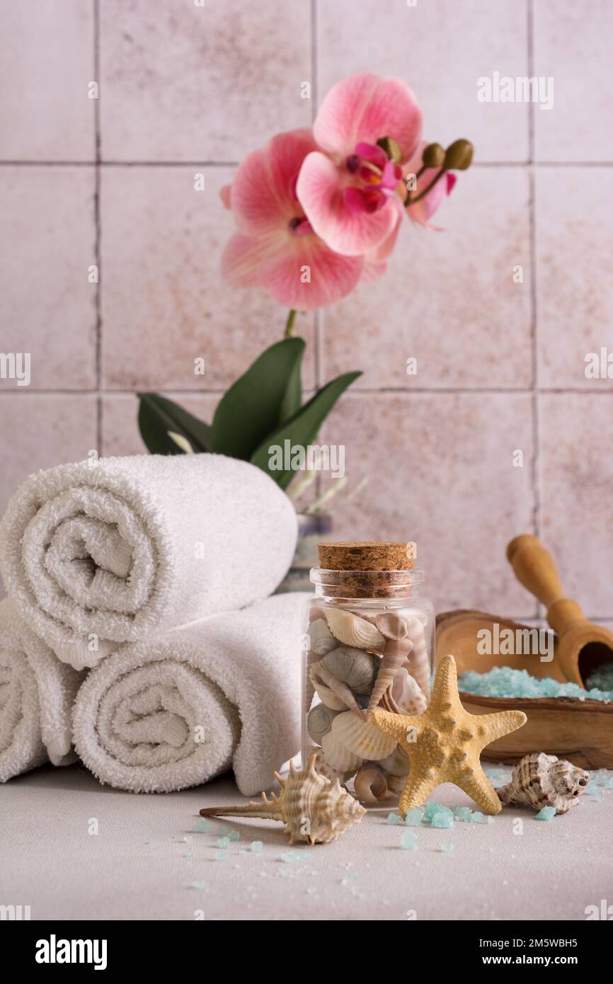 Blaues Meersalz in einer Holzschüssel mit Muscheln, Orchideenblume und weißen Handtüchern zum Entspannen, Bad, Spa auf gefliestem Hintergrund Stockfoto