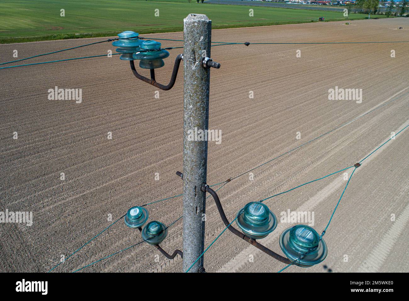 Luftaufnahme eines Stromleitungspols mit Glasisolatoren über Kulturfeld. Infrastruktur und Landwirtschaft. Stockfoto