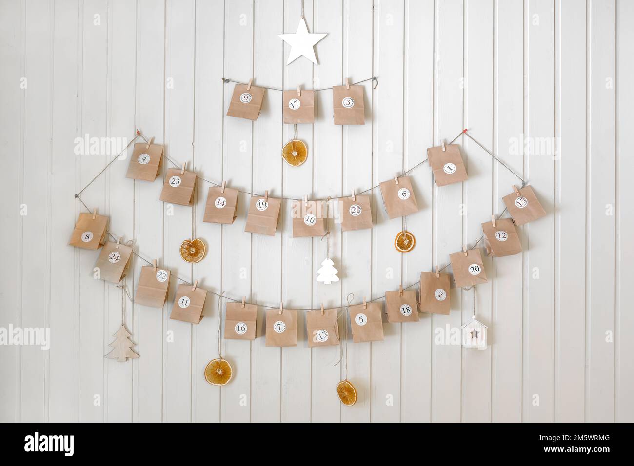 Adventskalender. Kleine handgemachte Papiergeschenke hängen auf dem Hintergrund einer Holzwand, Nahaufnahme. Weihnachtskalender, Geschenk für Kinder. HEIMWERKER. Sustainabl Stockfoto