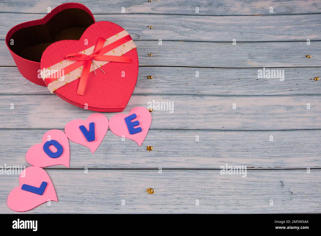 Rote herzförmige Box auf einem blauen Holztisch, mit ein paar Herzen mit dem Wort Liebe. Stockfoto