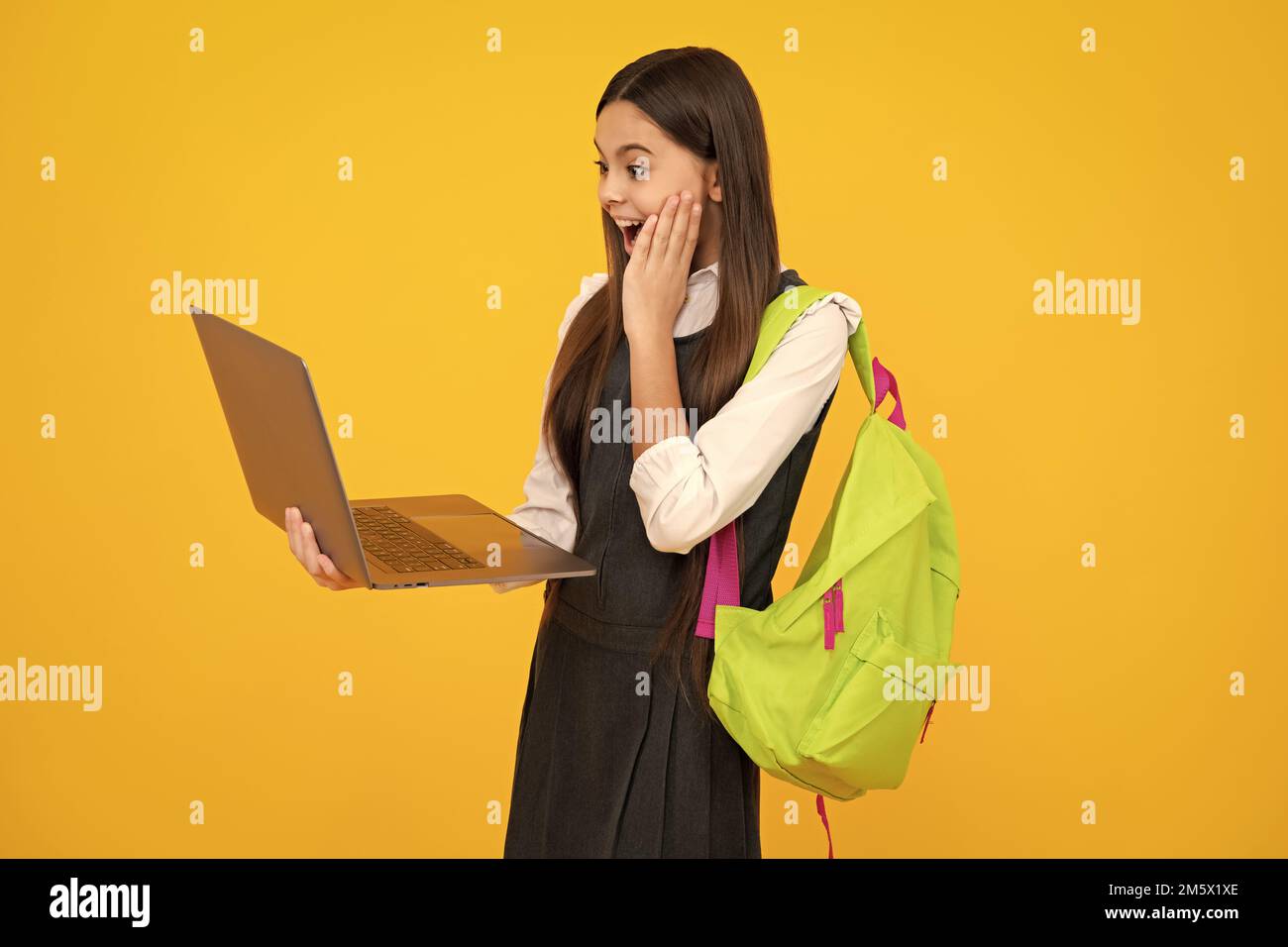 Schulmädchen in Schuluniform mit Laptop. Schülerin, Teenager-Schülerin auf gelbem isolierten Hintergrund. Aufgeregt Gesicht, fröhliche Emotionen von Teenager-Mädchen. Stockfoto