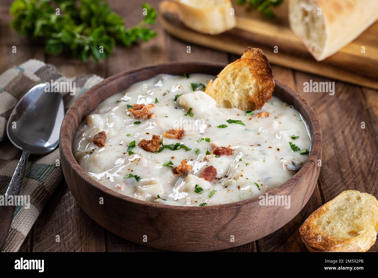 Muschelsuppe aus neuengland mit Speck, Petersilie und getoastetem französischem Brot in einer Holzschüssel Stockfoto