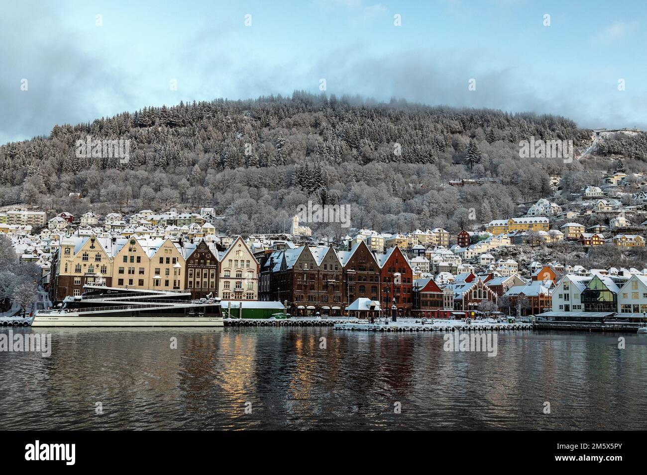 Aus einem Teil von Bryggen, dem alten Hafengebiet von bergen, Norwegen. Besichtigungsschiff Vision of the Fjords. Mount Floyen im Hintergrund. Eine dunkle, wi Stockfoto
