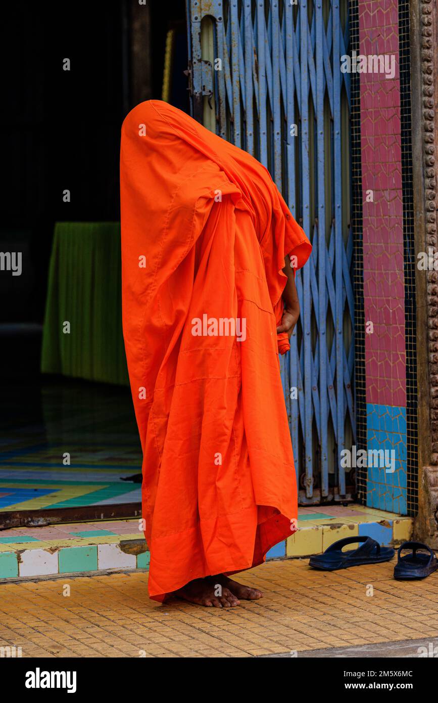 Ein junger Anfängermönch ist vollständig von seinem leuchtend orangefarbenen Morgenmantel bedeckt, während er zeigt, wie er sich anzieht Stockfoto