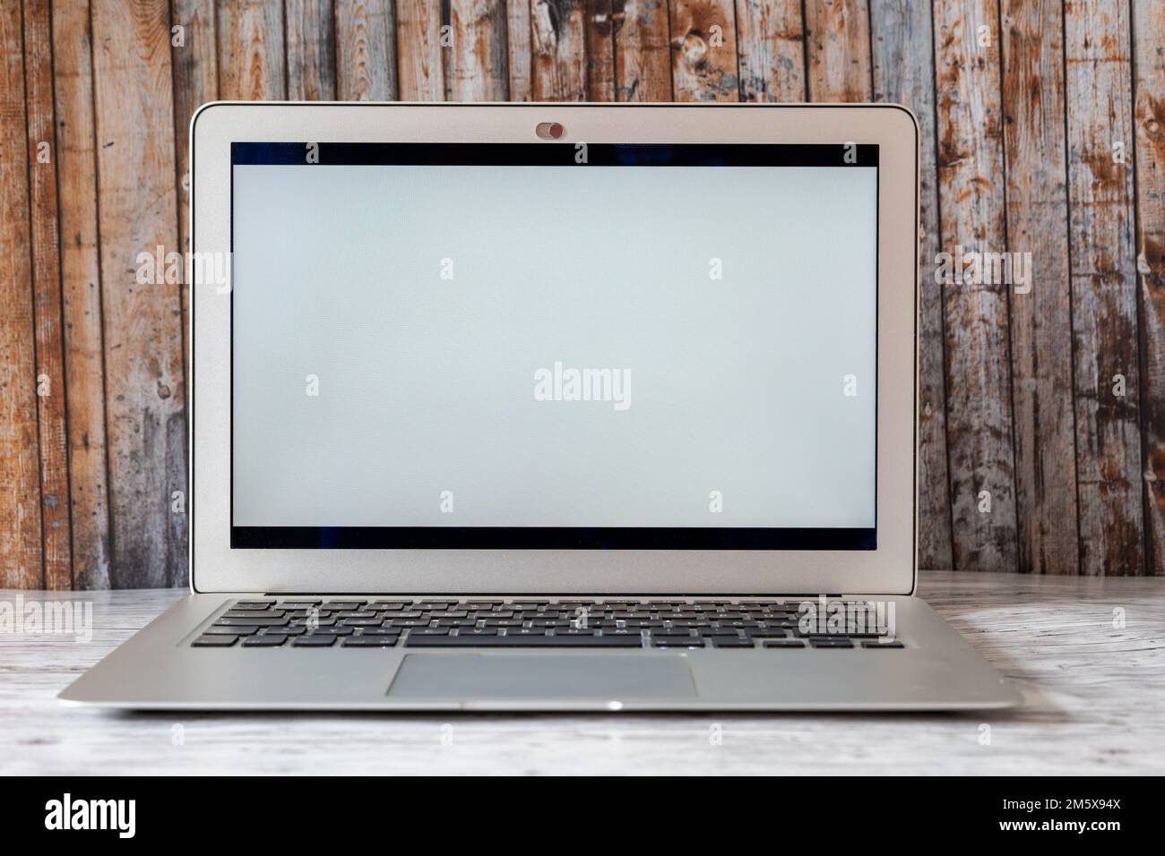 Nahaufnahme eines Laptops mit leerem Bildschirm und Holzwandhintergrund, Online-Technologie-Konzept Stockfoto