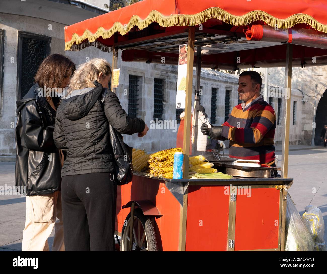 Frauen kaufen bei Händlern. Ein Händler, der Mais auf dem Eminonu-Platz verkauft. Istanbul - Türkei - 31. Dezember 2022. Stockfoto