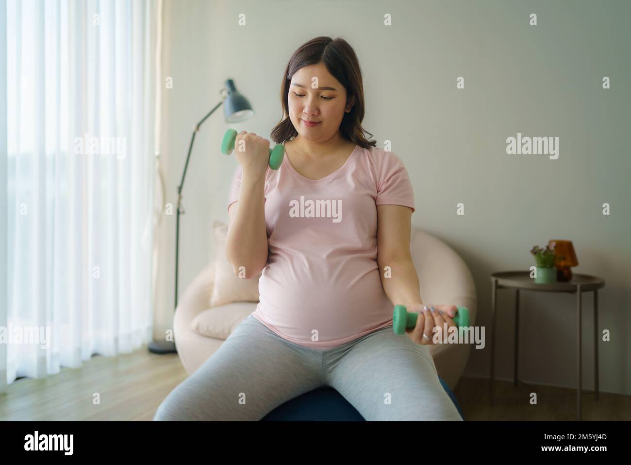 Schöne asiatische schwangere Frau, die zu Hause mit Kurzhanteln trainiert, gesundes Konzept Stockfoto
