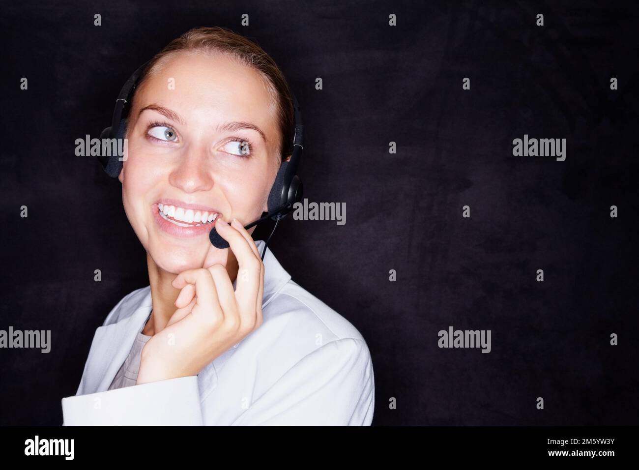 Glückliche Geschäftsfrau mit einem Headset auf Schwarz. Lächelnde junge Geschäftsfrau mit einem Headset, isoliert vor schwarzem Hintergrund. Stockfoto