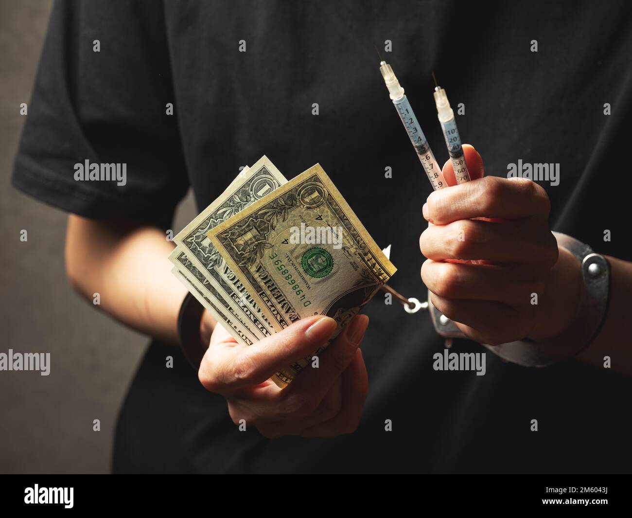 Handschellen an Handgelenken, Dollarscheine und Spritze Stockfoto