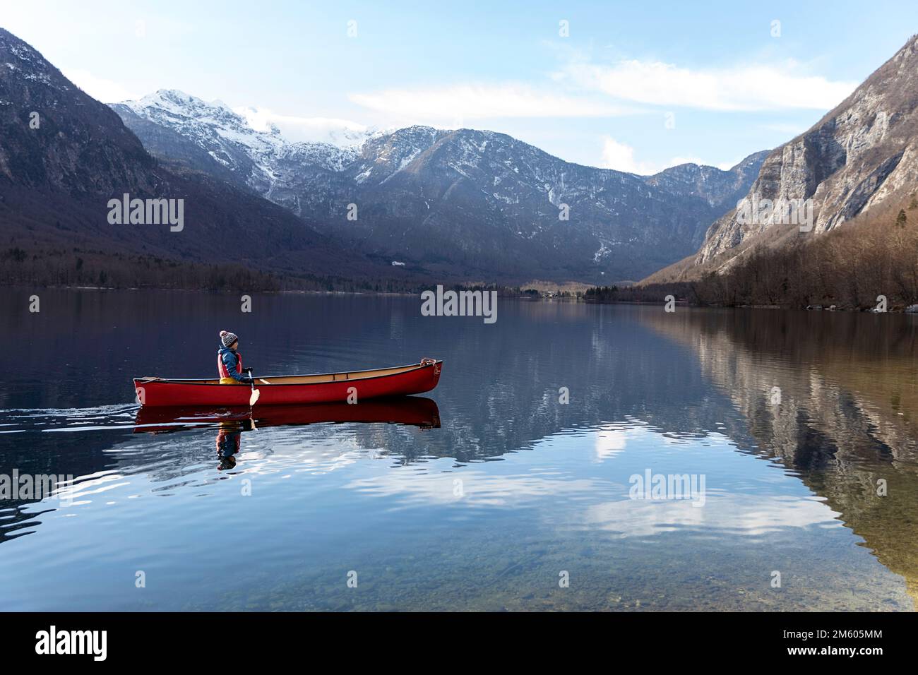Einheimisches Kind paddelt in einem roten Kanu an einem kalten Wintertag auf einem ruhigen und schönen See Bohinj in Gorenjska in Slowenien Stockfoto