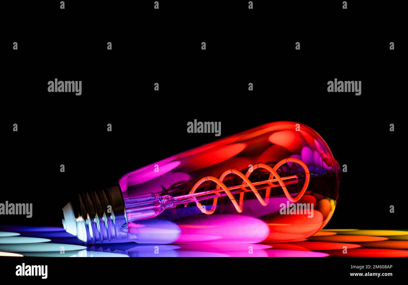 Bunte Muster spiegeln sich in einer ovalen Glühbirne aus klarem Glas wider, die vor schwarzem Hintergrund fotografiert wird Stockfoto
