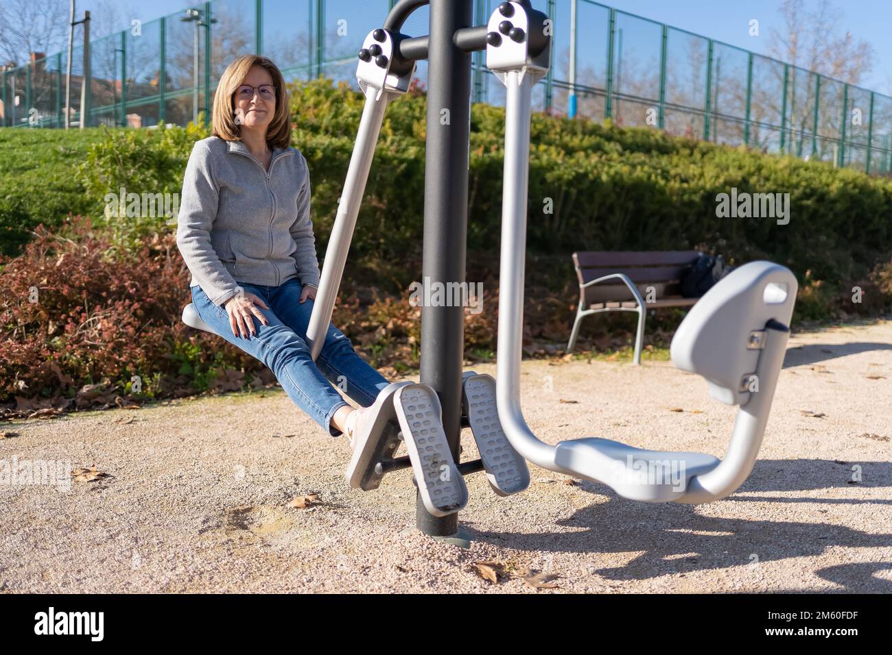 Reife Frau, die mit ihren Beinen in einem Gymnastikapparat in einem öffentlichen Park Sport macht. Stockfoto