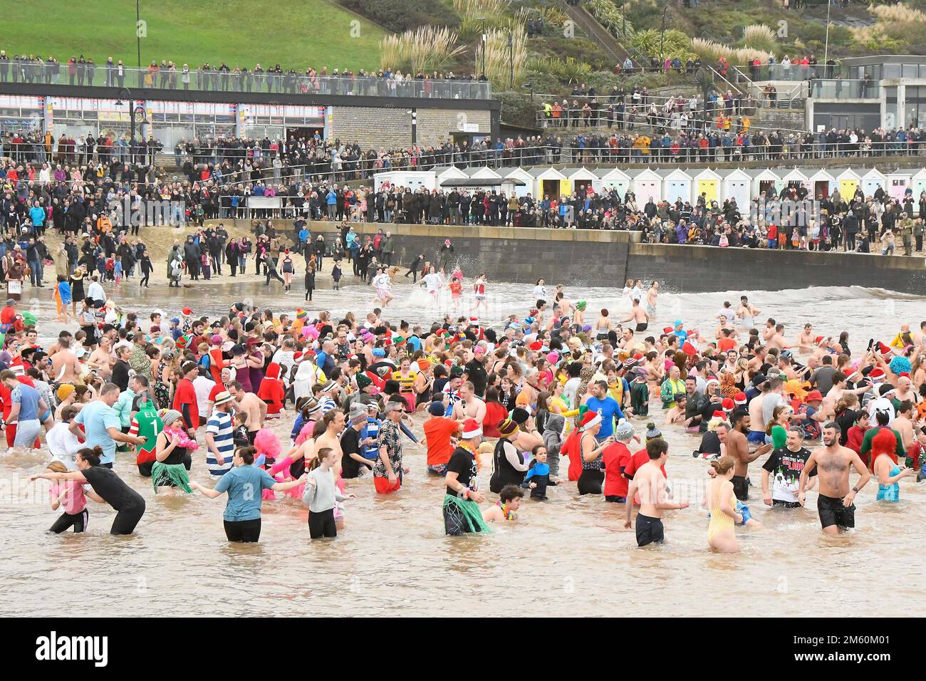 Lyme Regis, Dorset, Großbritannien. 1. Januar 2023 Hunderte von Neujahrsfeierern in schicken Kleidern, beobachtet von riesigen Menschenmassen, nehmen an einem bedeckten feuchten Tag am jährlichen Lyme Lunge-Schwimmen im Lyme Regis in Dorset Teil, um Mencap und der National Heart Foundation zu helfen. Bildnachweis: Graham Hunt/Alamy Live News Stockfoto