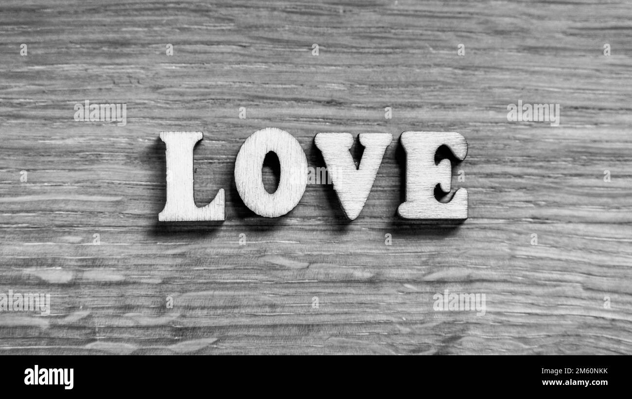 Love - Wortinschrift von 3D Holzbuchstaben auf dem holzstrukturierten Boardhintergrund. Ausdruck von romantischem Thema oder Valentinstag. Rustikale Inschrift. Schwarzweißbild. Stockfoto