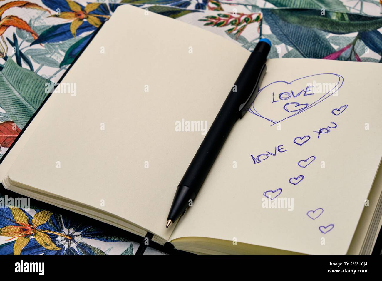 Öffne das Tagebuch mit einem Stift und schreibe das Wort Liebe auf einen Tisch mit einem tropischen Muster. Stockfoto