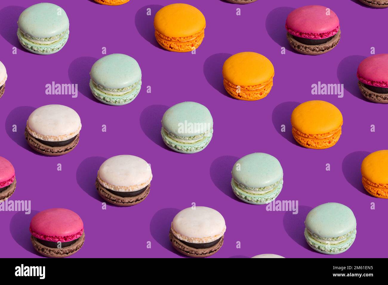 Bunte Makronen auf dunkellila Hintergrund. Sommerliches Muster süßer Speisen. Ästhetisches Stillleben-Konzept. Trendige Farben mit starkem Kontrast. Stockfoto