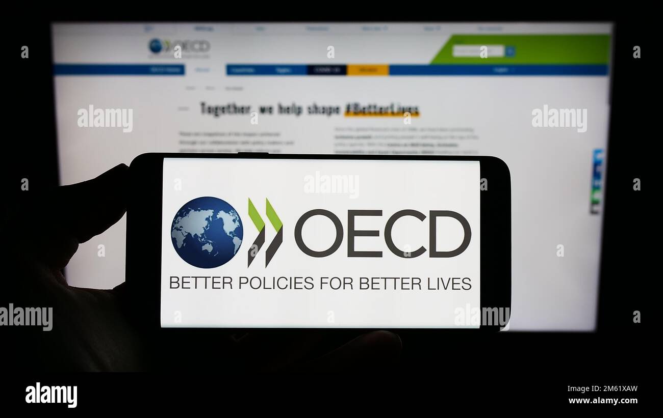 Person, die ein Mobiltelefon mit dem Logo der zwischenstaatlichen Organisation OECD auf dem Bildschirm vor der Webseite hält. Konzentrieren Sie sich auf das Display des Telefons. Stockfoto