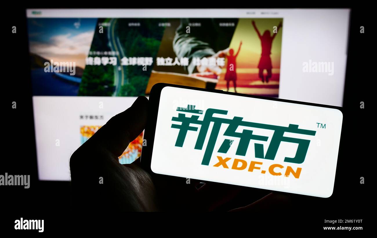 Person, die ein Smartphone mit dem Logo der New Oriental Education and Technology Group auf dem Bildschirm vor der Website hält. Konzentrieren Sie sich auf das Display des Telefons. Stockfoto