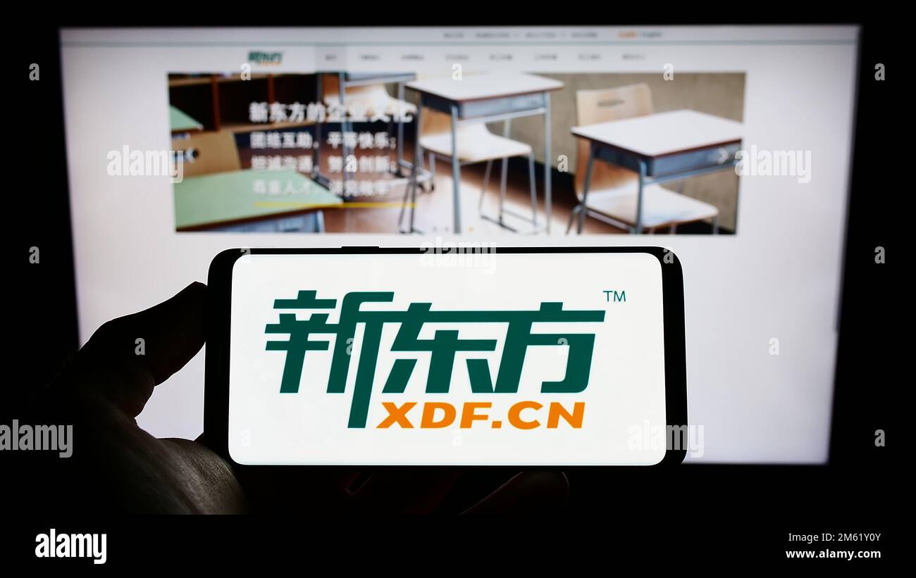 Person, die ein Mobiltelefon mit dem Logo der New Oriental Education and Technology Group auf dem Bildschirm vor der Webseite hält. Konzentrieren Sie sich auf das Display des Telefons. Stockfoto