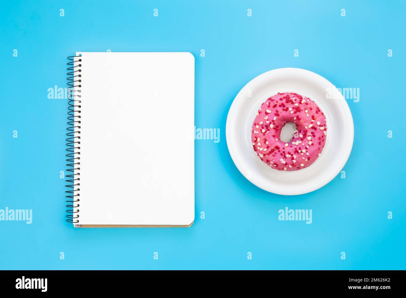 Leerer Notizblock und Donut auf blauem Hintergrund, flach liegend. Stockfoto