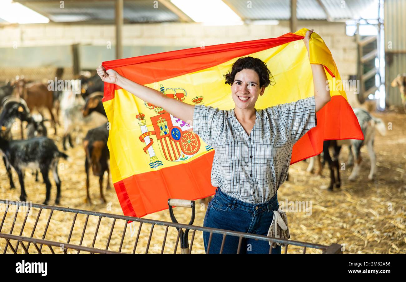 Glückliche Landwirtin im Ziegenschuppen mit spanischer Flagge Stockfoto