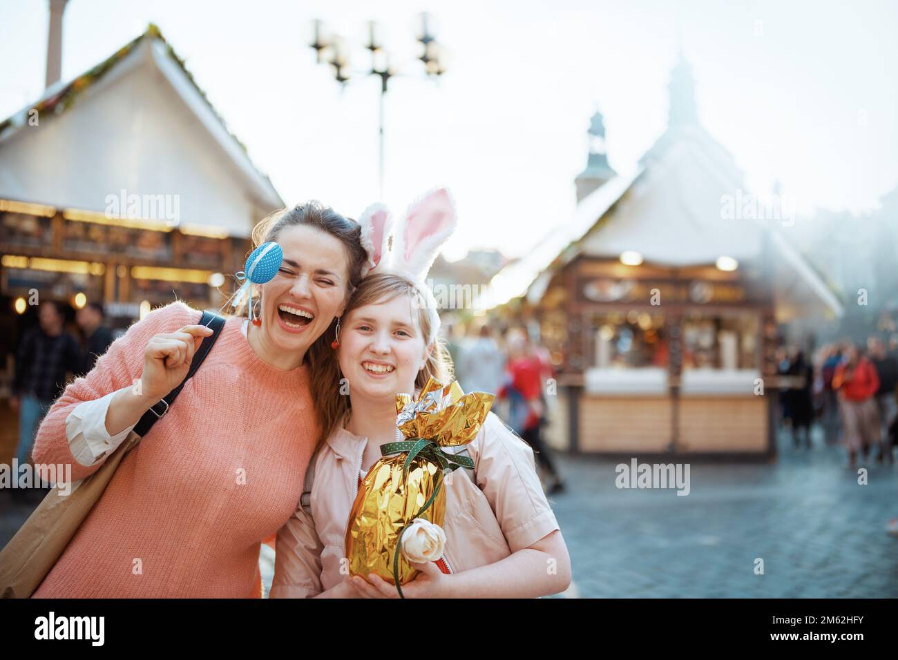 Osterspaß. Lächelnde junge Mutter und Kind mit goldenem osterei auf dem Jahrmarkt in der Stadt. Stockfoto