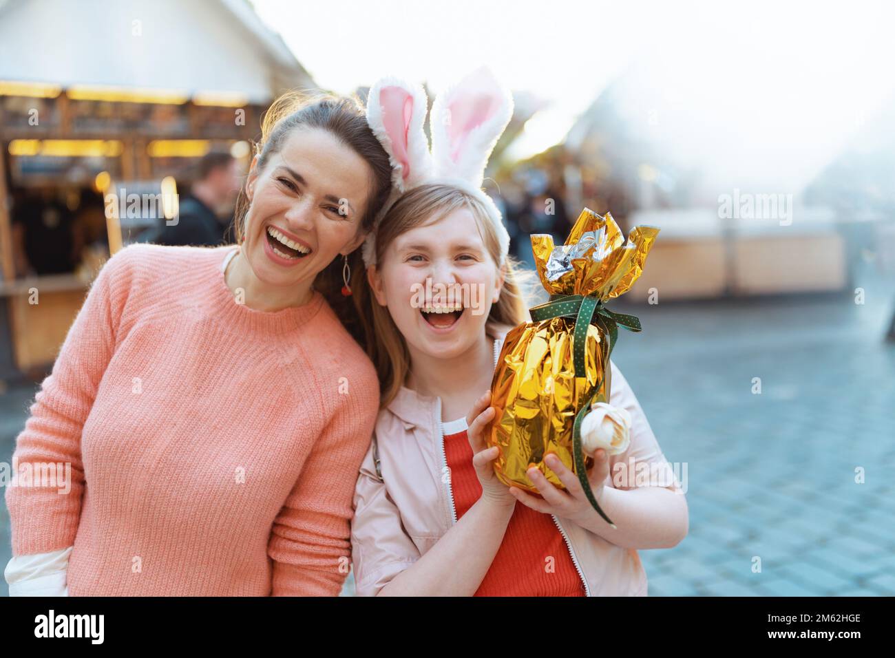 Osterspaß. Glückliche kleine Mutter und Kind mit goldenem osterei auf dem Jahrmarkt in der Stadt. Stockfoto