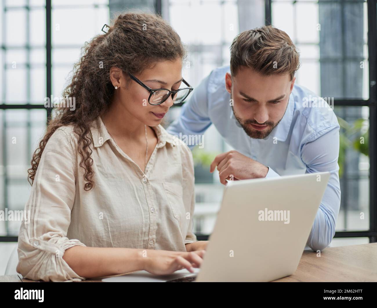 Eine Geschäftsfrau, die mit ihrem Kollegen im Büro auf ein Notebook schaut Stockfoto