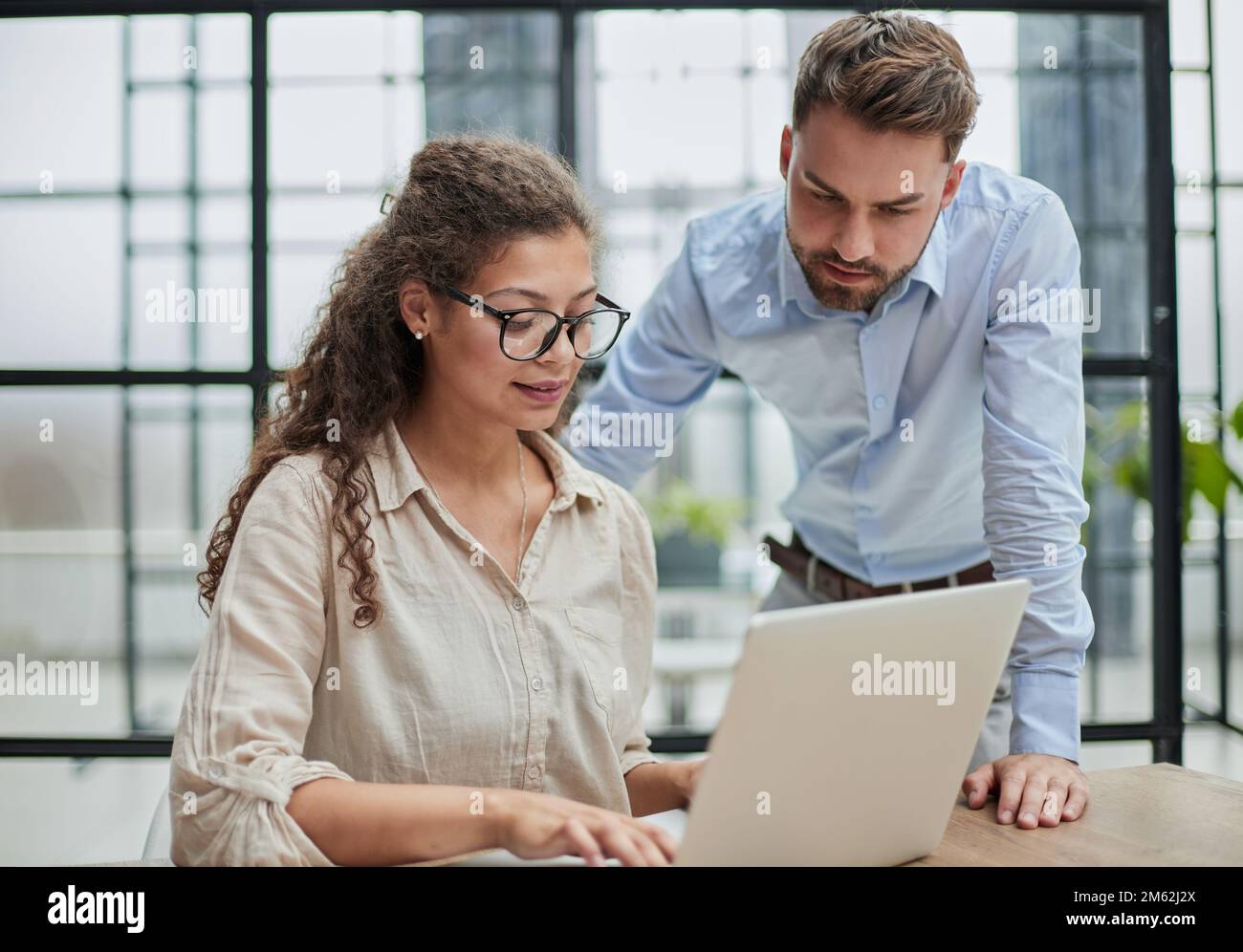 Eine Geschäftsfrau, die mit ihrem Kollegen im Büro auf ein Notebook schaut Stockfoto