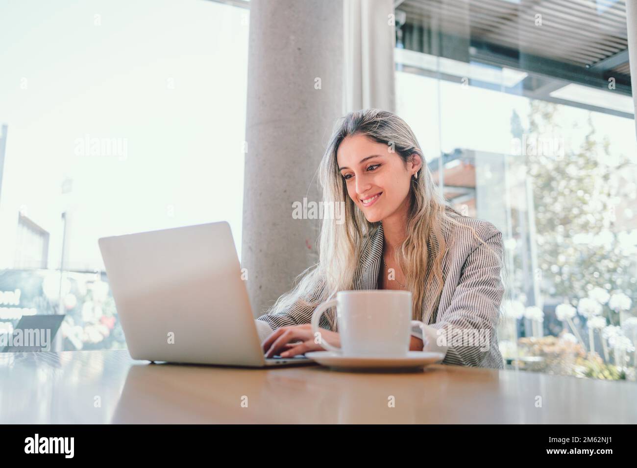 Ruhige Geschäftsfrau der Millennials, die ein Notebook benutzt, mit einer Tasse Kaffee am modernen Arbeitsplatz. Stockfoto