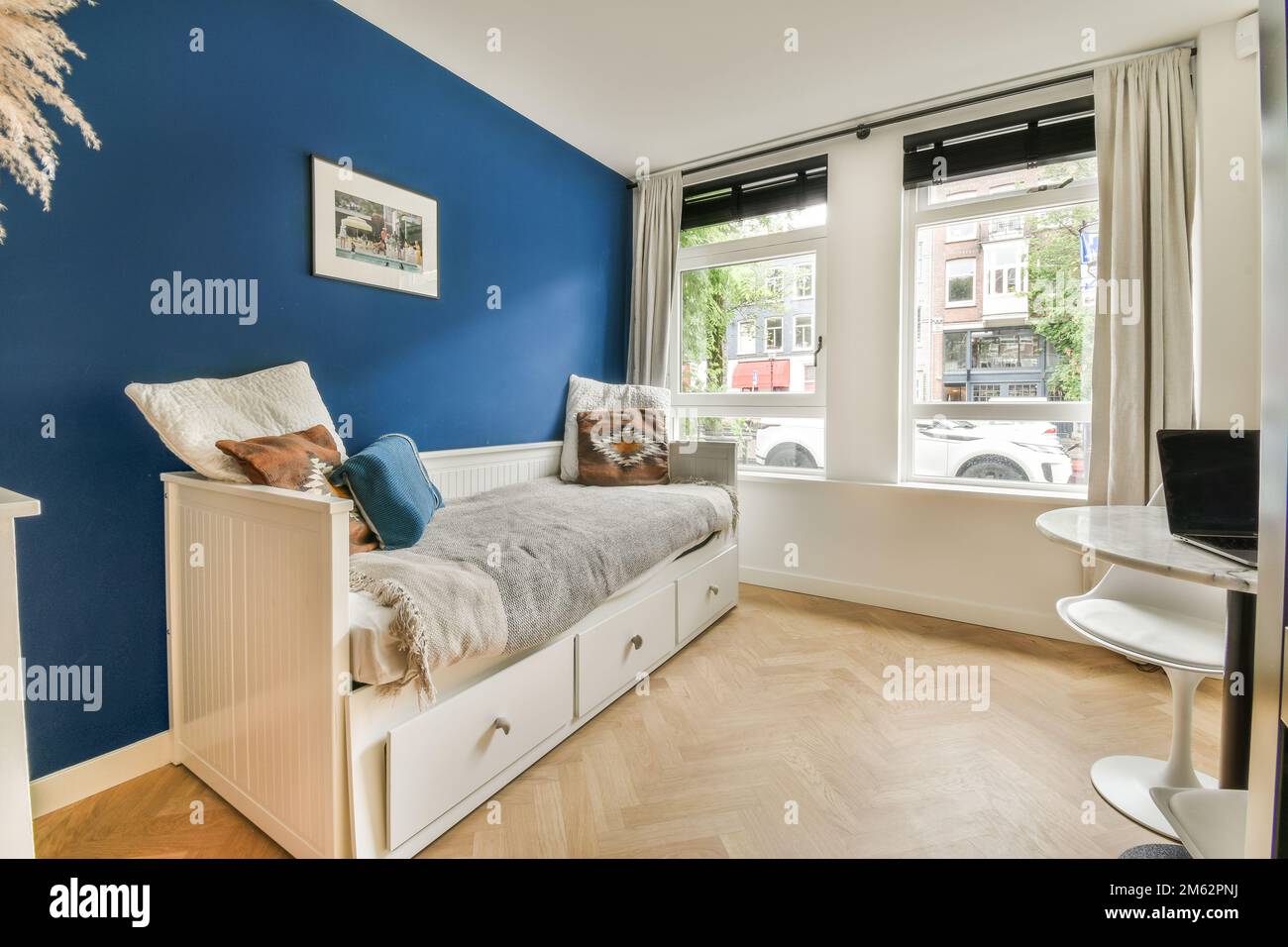 Ein Kinderzimmer mit blauen Wänden und weißen Möbeln, einschließlich eines kleinen Betts vor dem Fenster Stockfoto