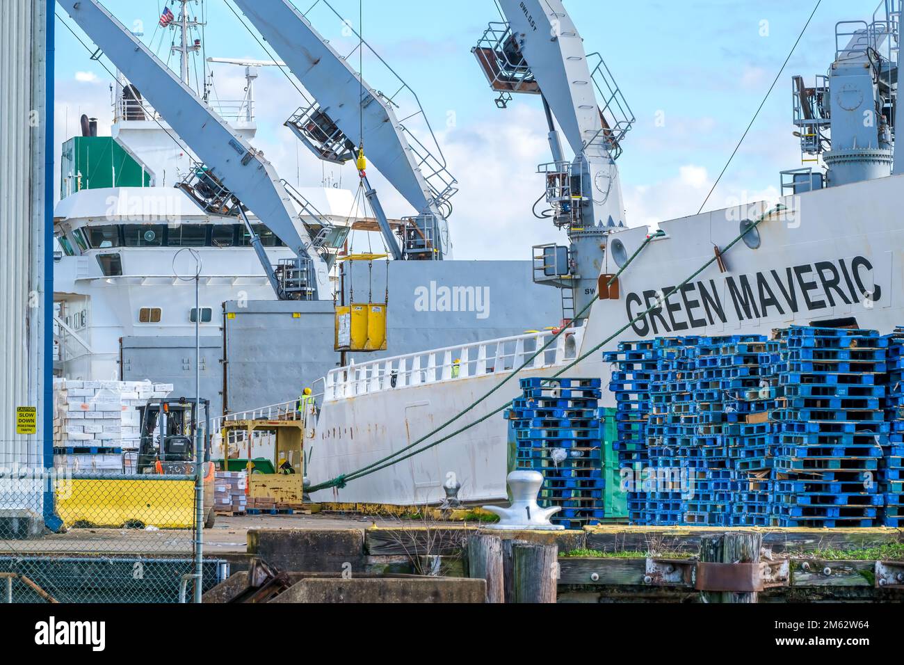NEW ORLEANS, LA, USA - 28. DEZEMBER 2022: Green Maveric Kühlfrachtschiff mit Kränen, die Fracht laden und Paletten am Kai stapeln Stockfoto