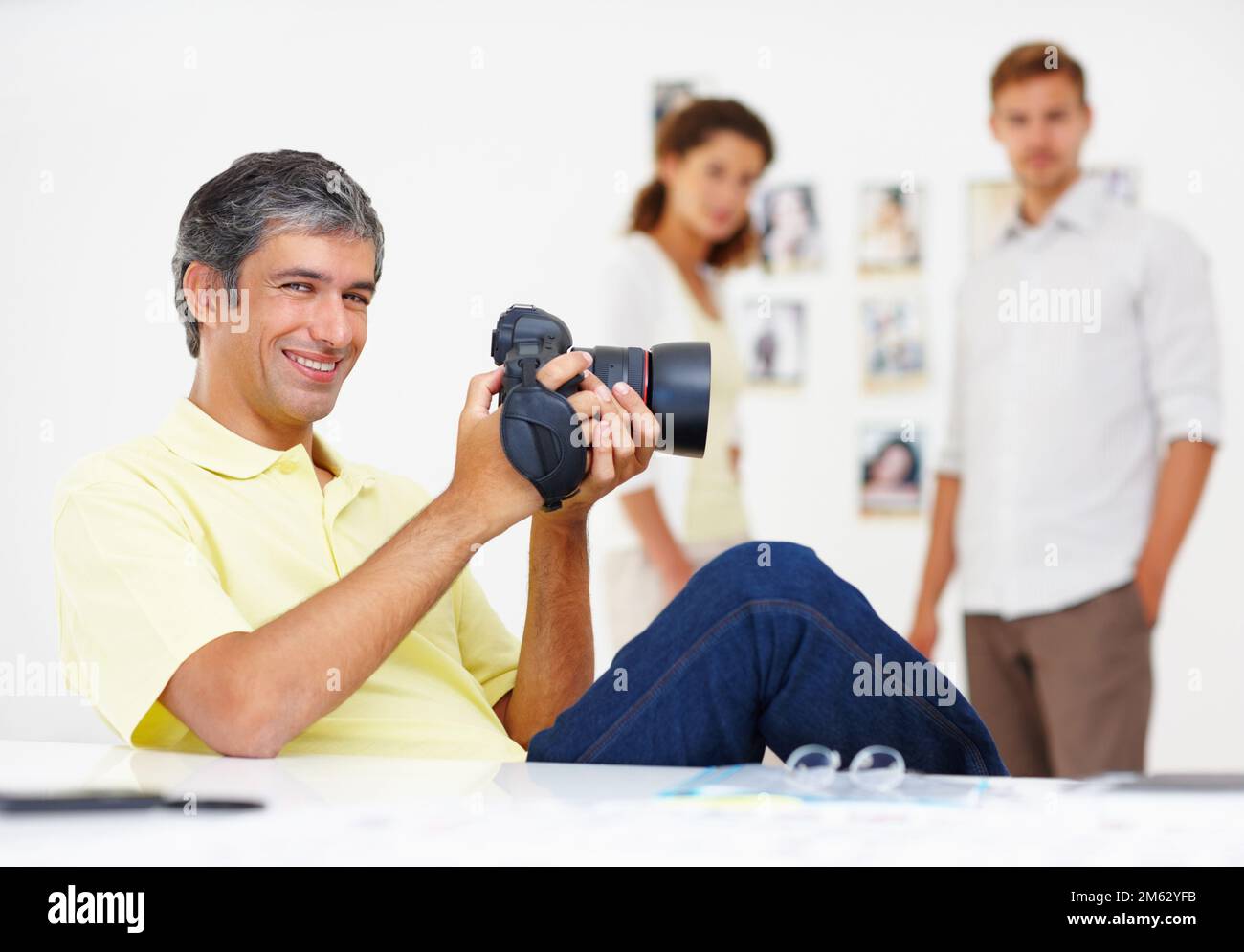Kluger Mann, der Bilder in der Kamera überprüft. Porträt eines cleveren Mannes, der Fotos in seiner Kamera mit Kollegen im Hintergrund ansieht. Stockfoto