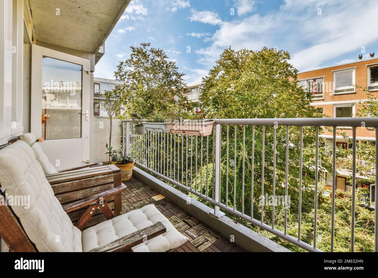 Ein Balkon mit weißen Möbeln und Bäumen im Hintergrund, vom oberen Stockwerk des Apartments aus, mit Blick auf die Fenster Stockfoto