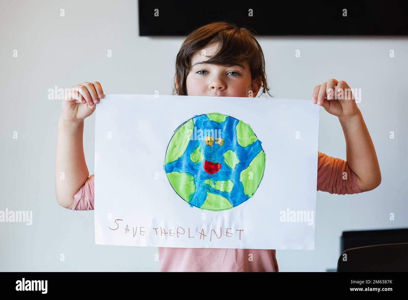 Ein Mädchen in legerer Kleidung, das Papier mit der Inschrift Erde und Save the Planet vorführt und im Klassenzimmer in die Kamera schaut Stockfoto