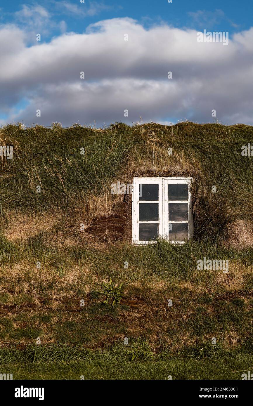 Außenansicht des isländischen Turfhauses mit kleiner weißer Witwe, bedeckt von einem Grasdach unter bewölktem Himmel Stockfoto