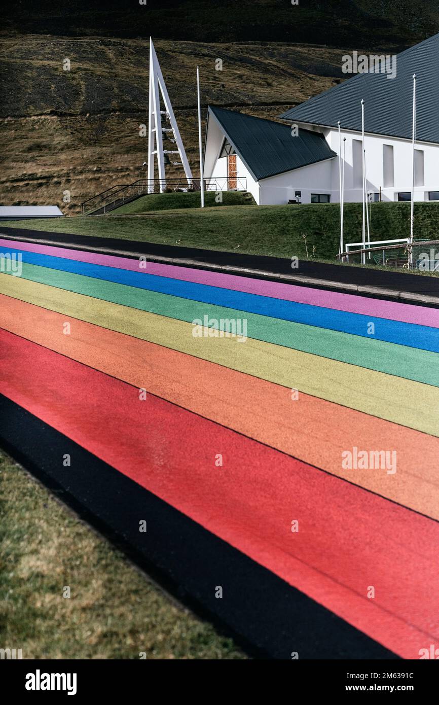 Leere Straße in LGBT-Flaggenfarben in Regenbogenfarben in der Nähe eines typischen Wohnhauses an sonnigen Tagen in Island Stockfoto