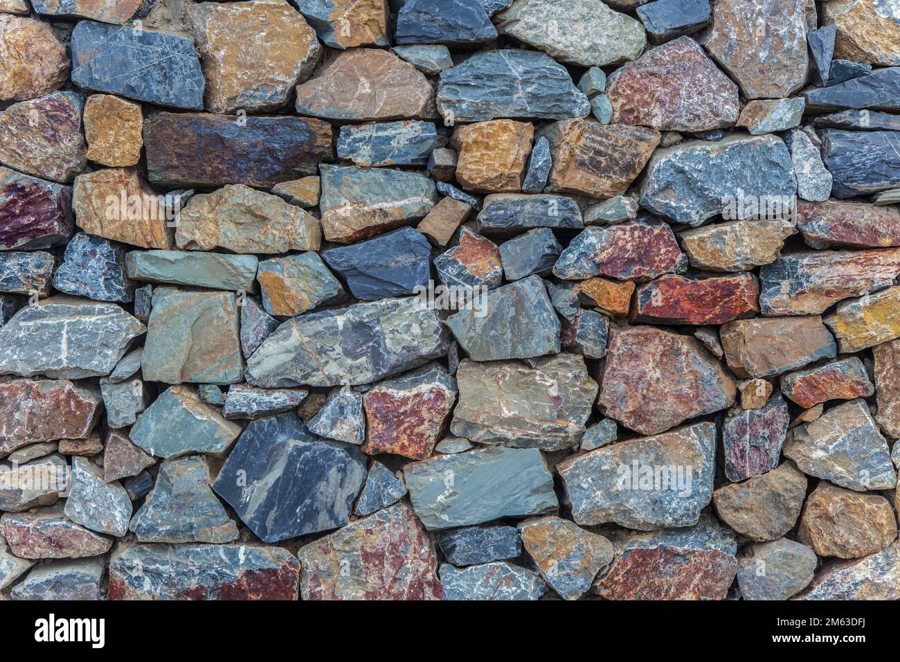 Natürliche, farbenfrohe rostfarbene Quarzitwand. Unregelmäßige Steine. Stockfoto
