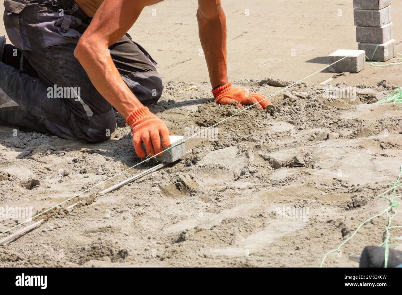Ein Arbeiter zieht an einem sonnigen Sommertag ein Nylonfaden, um Pflasterplatten zu legen. Speicherplatz kopieren. Stockfoto