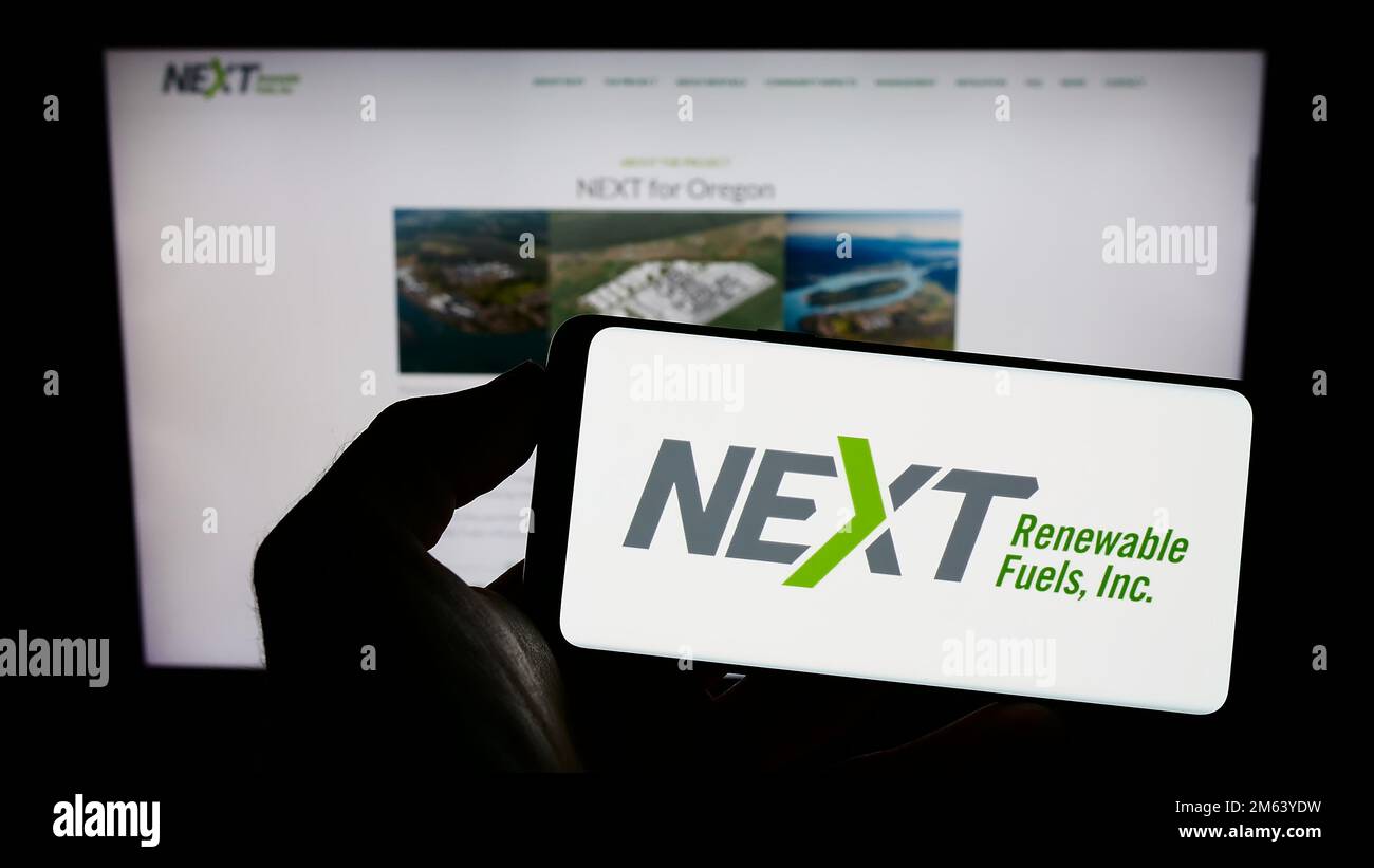 Person, die ein Mobiltelefon mit dem Logo des US-Unternehmens NEXT Renewable Fuels Inc. Auf dem Bildschirm vor der Unternehmenswebseite hält. Konzentrieren Sie sich auf das Display des Telefons. Stockfoto