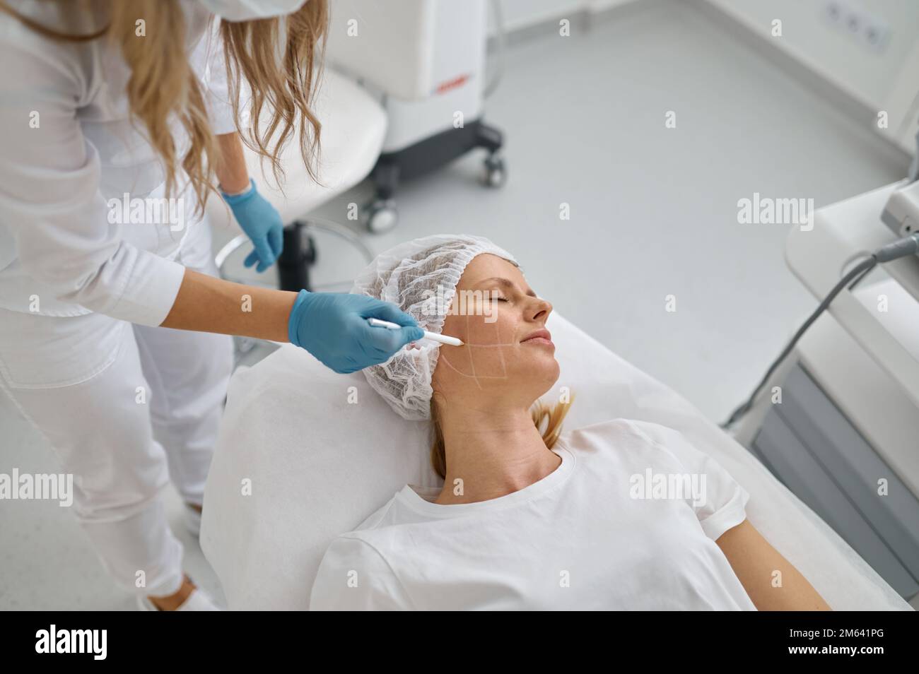 Kosmetologe zeichnen mit weißem Bleistift auf dem Gesicht des Patienten Stockfoto