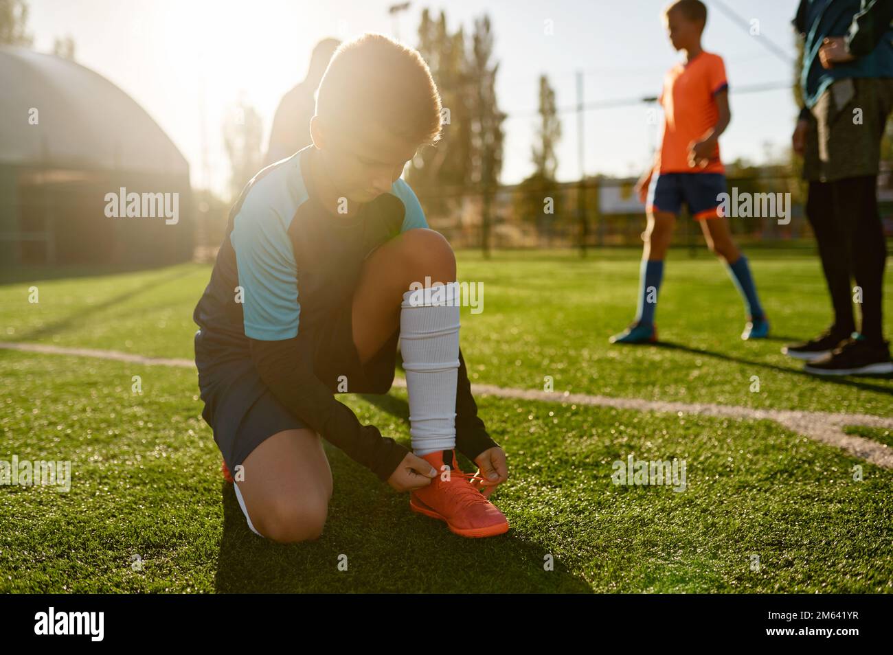 Ein kleiner Footballspieler, der Schnürsenkel bindet und auf dem Fußballfeld sitzt Stockfoto
