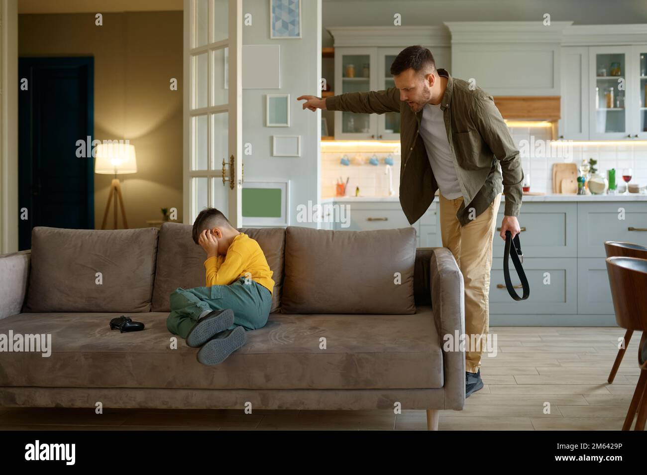 Vater mit Ledergürtel schreit auf Sohn, der Computervideospiele spielt Stockfoto