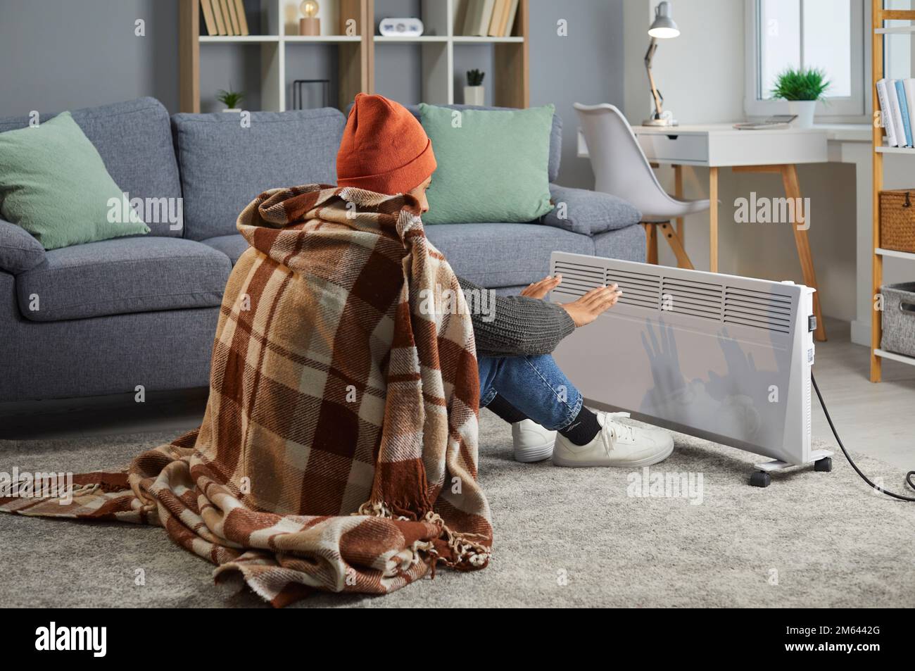 Die junge Frau versucht, sich im Winter mit einem elektrischen Heizgerät in einem Kühlhaus aufzuwärmen Stockfoto