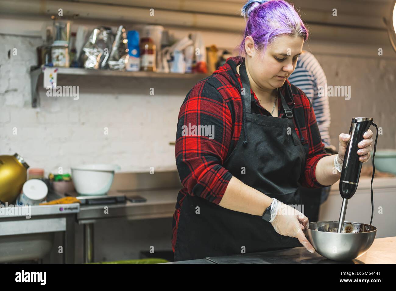 Fokussierter weißer Konditor, der den Teig mit einem Stabmixer oder Mixer in einer Edelstahlschüssel mischt. Kücheneinrichtung. Hochwertiges Foto Stockfoto