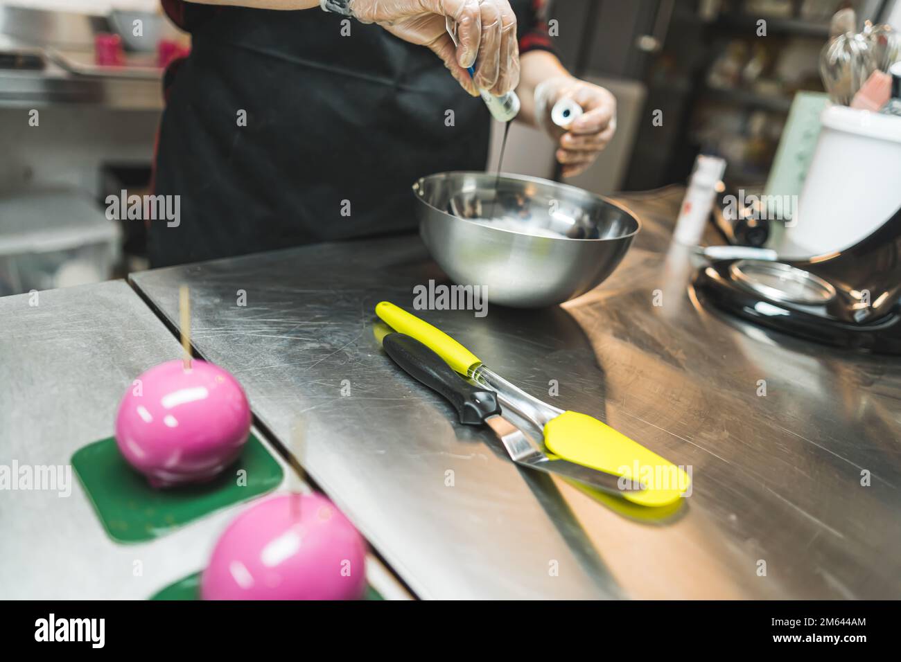 Geräte für die Kuchendekoration. Person, die Buttercreme-Glasur mit Lebensmittelfarbe in einer Stahlschüssel zubereitet. Hochwertiges Foto Stockfoto