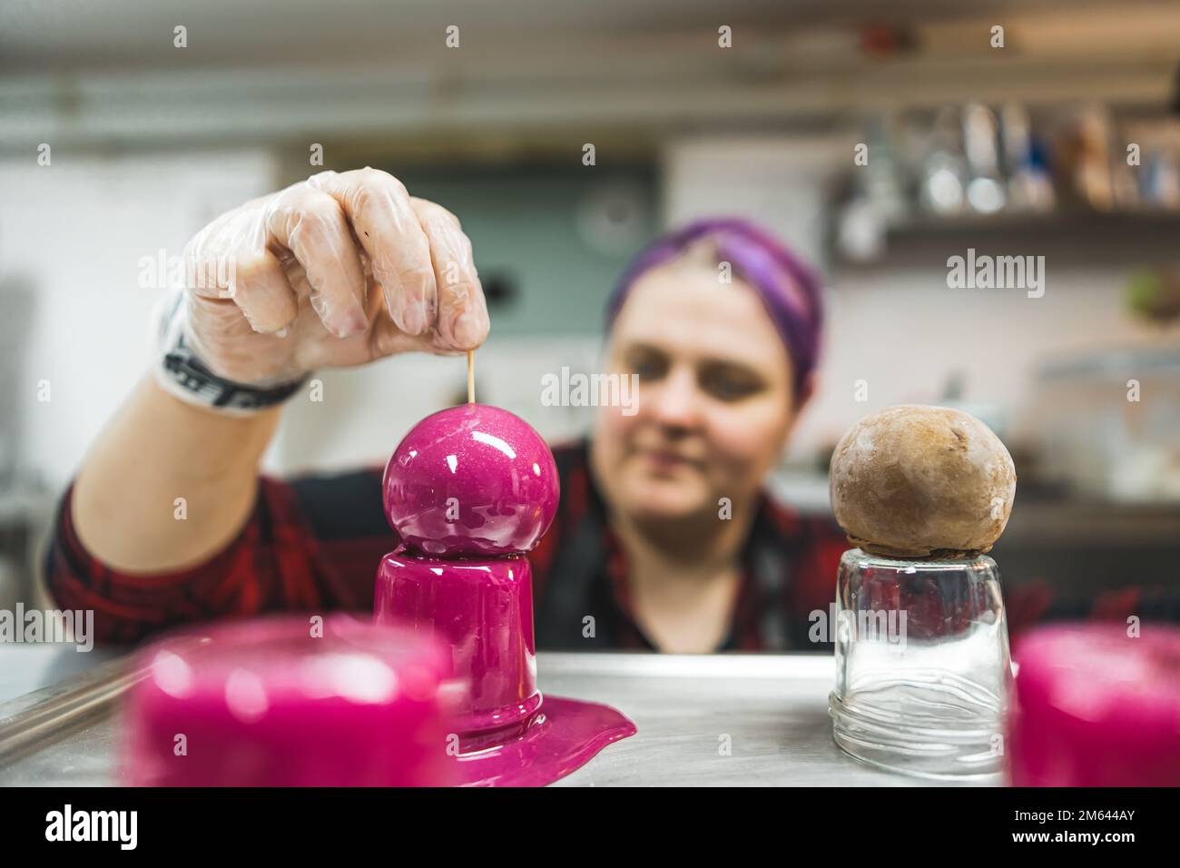 Lebensmittelfarben und Kuchendekoration. Praline mit leuchtend rosafarbener Glasur bedeckt. Verschwommener Konditor im verschwommenen Hintergrund. Hochwertiges Foto Stockfoto