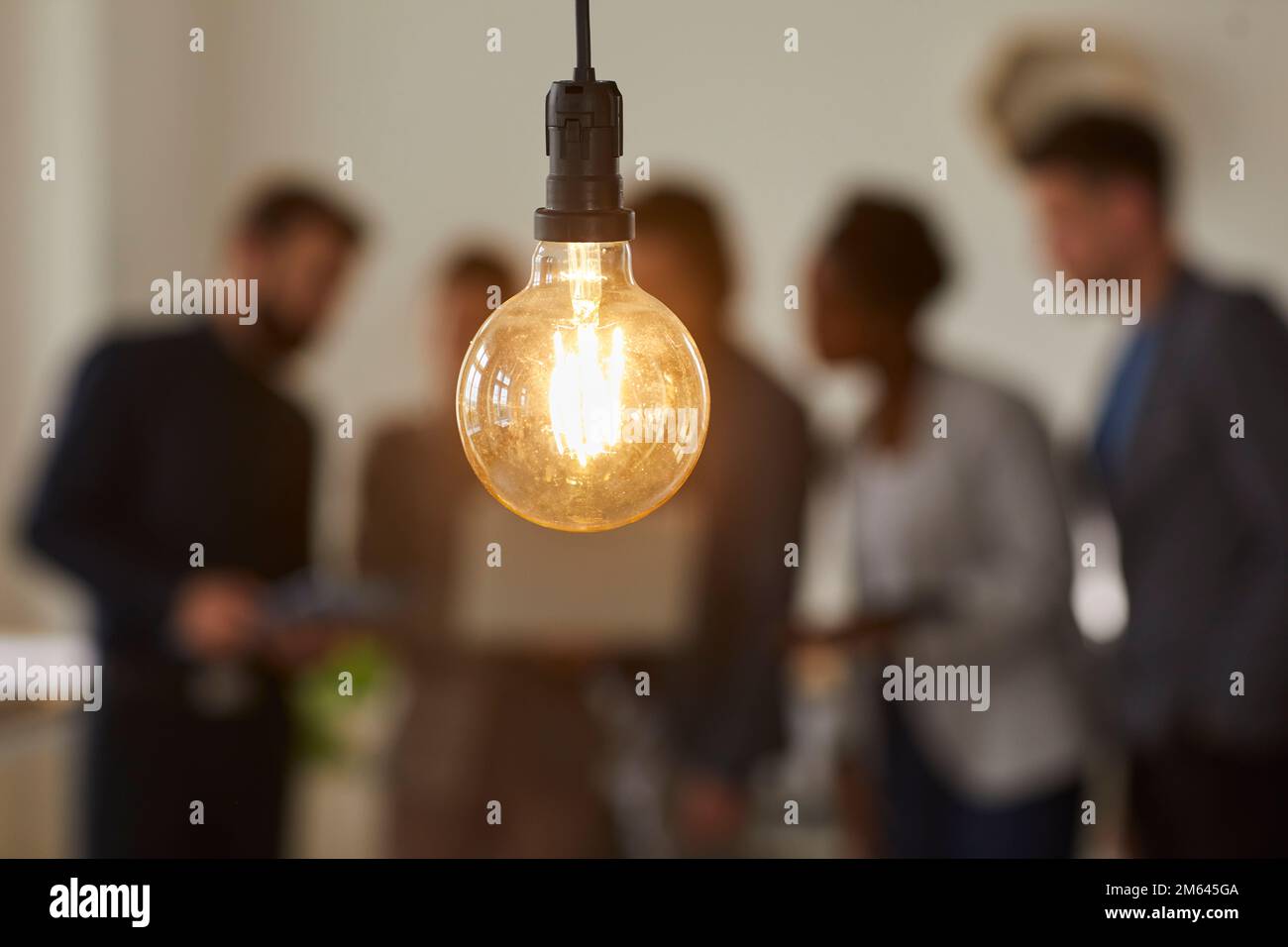 Glühbirne und Geschäftsleute auf unscharfem Hintergrund Stockfoto